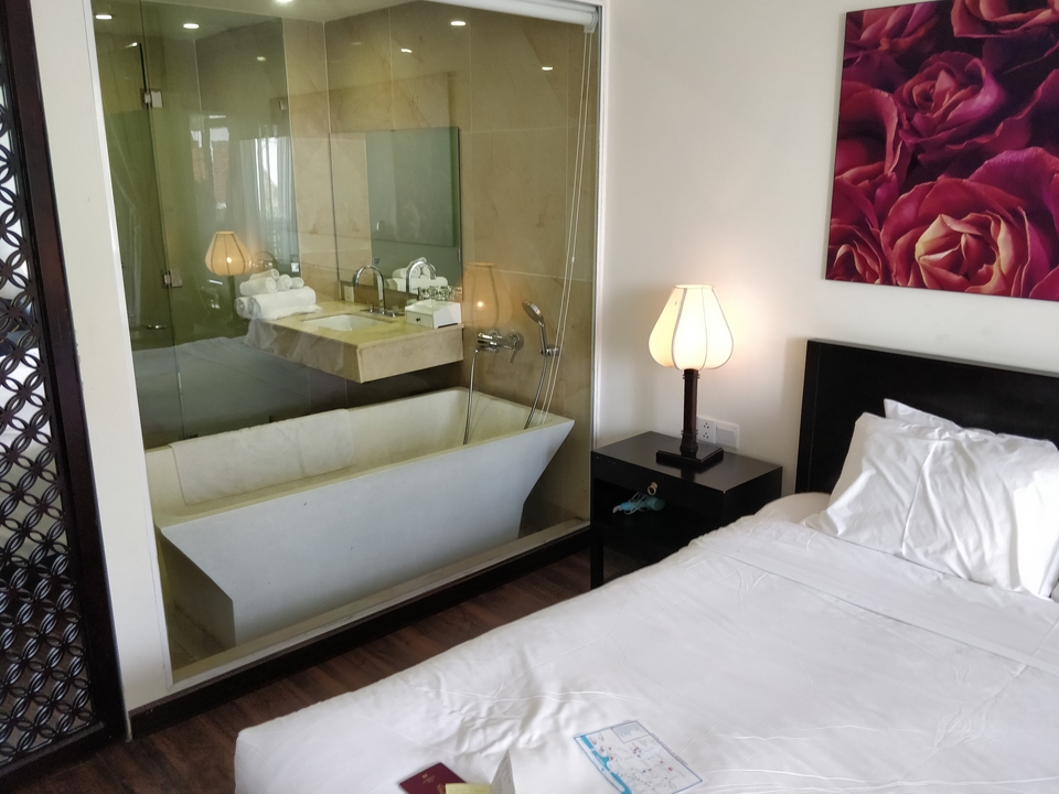 Intérieur de chambre d'hôtel avec un lit et une baignoire séparés par une cloison en verre.