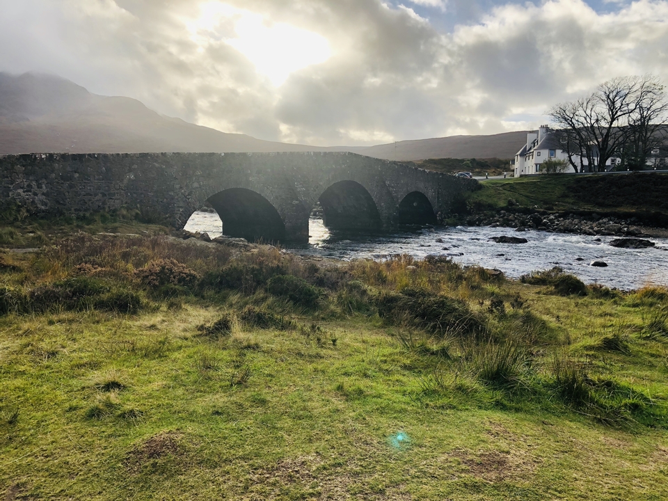 Pont de pierre avec une rivière et une maison en arrière-plan.