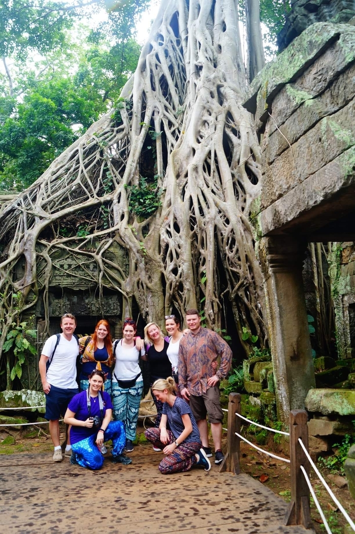 Groupe de personnes posant devant des ruines antiques avec de grandes racines d'arbres.