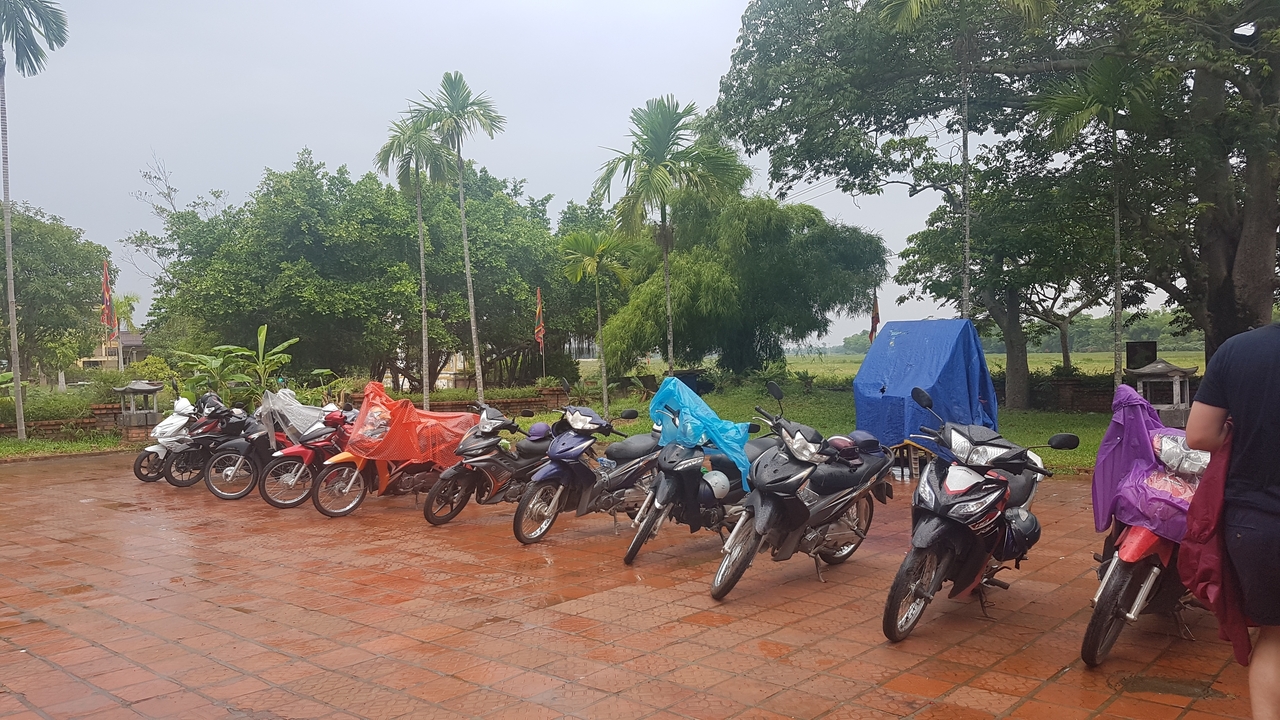 Rangée de motos recouvertes de protections anti-pluie garées sur une zone pavée.