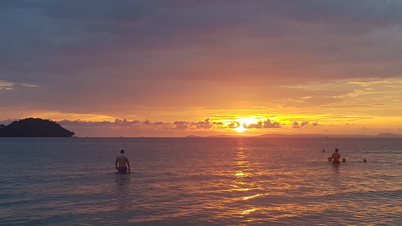 Coucher de soleil sur l'océan avec des gens qui nagent.