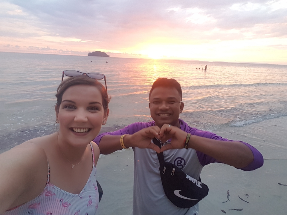 Deux personnes faisant un geste de cœur sur la plage au coucher du soleil.