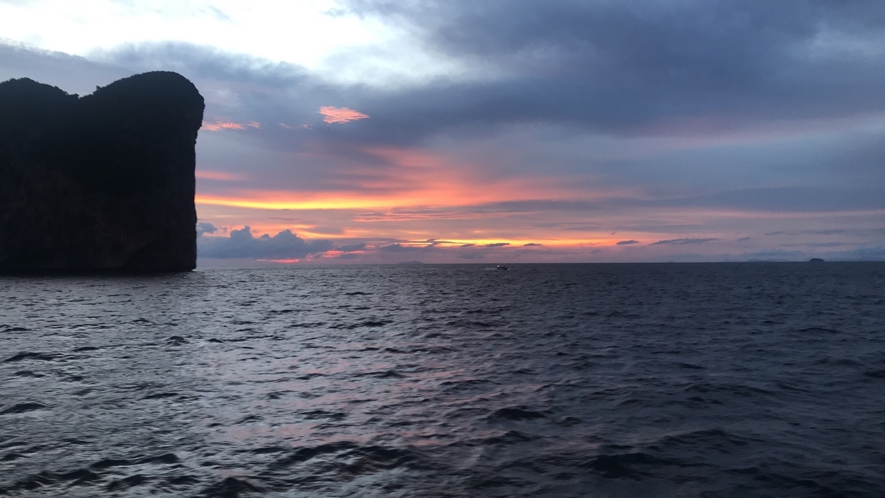 Océan au coucher du soleil avec un ciel dramatique et une silhouette de falaise.