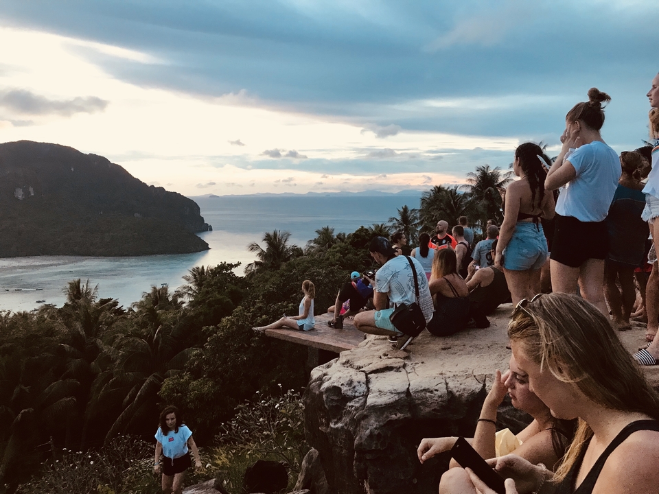 Foule de gens sur un point de vue surplombant la mer et les montagnes.