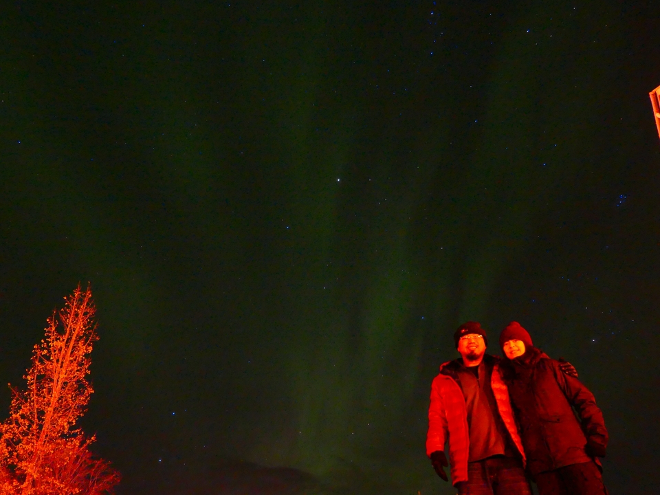 Two people standing under the northern lights against a starry night sky.