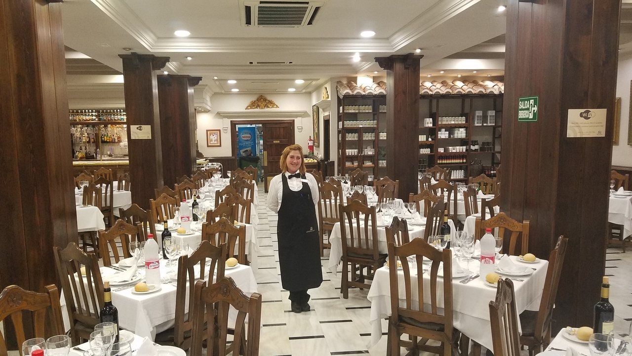 Femme debout dans une salle à manger préparée avec des tables et des chaises.