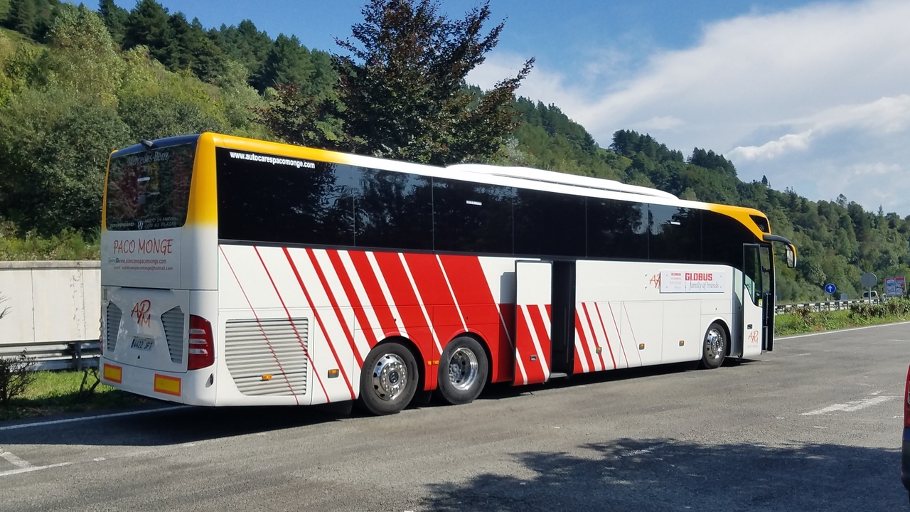 Autocar de tourisme garé sur une route avec des arbres et des collines en arrière-plan.