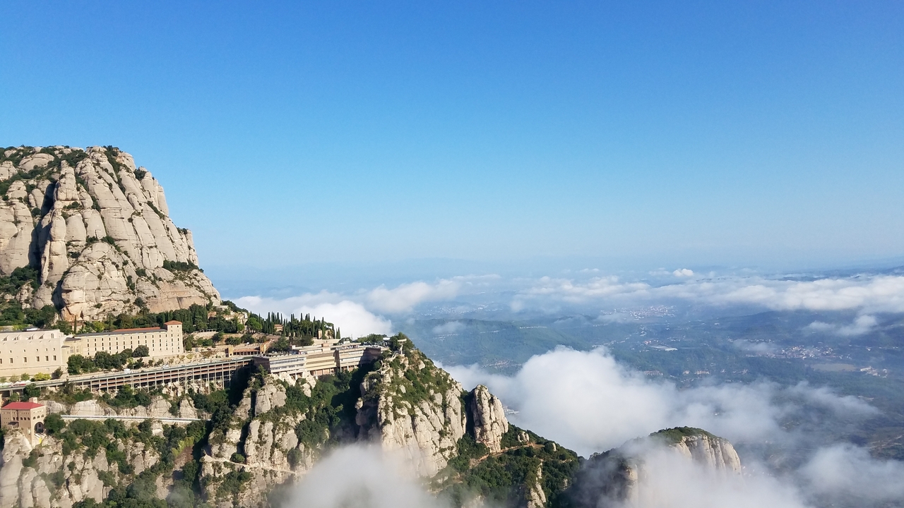 Vue aérienne du monastère de Montserrat sur une montagne entourée de nuages.