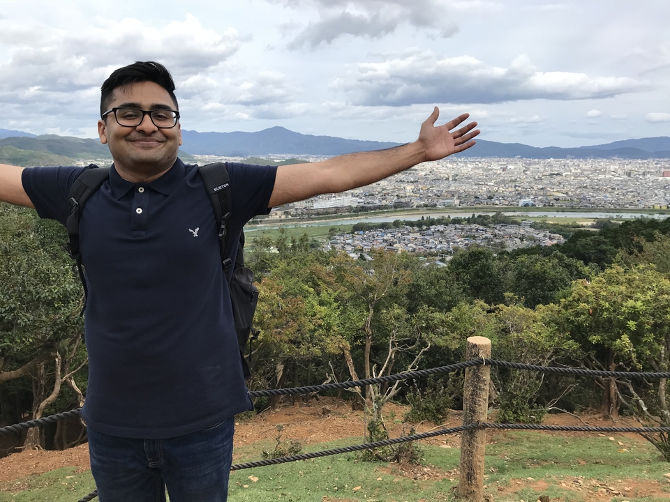 Homme posant avec vue sur une ville et des montagnes.