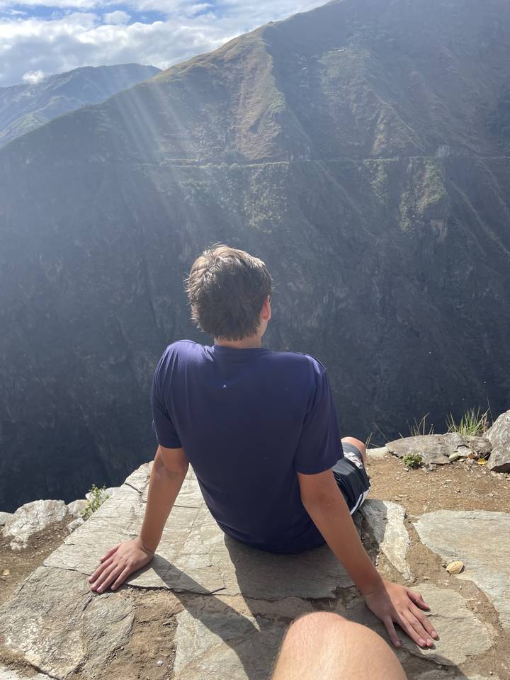 Personne assise près du bord d'un rocher avec une vue panoramique sur les montagnes.