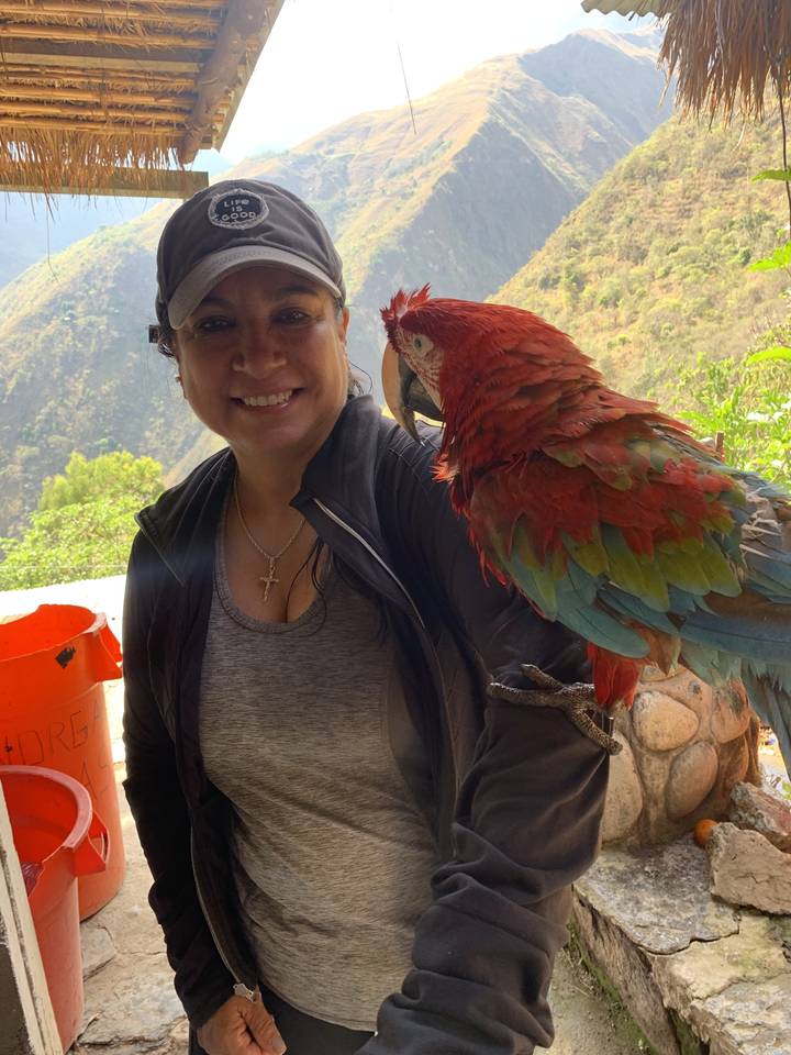 Femme souriante avec un perroquet perché sur son épaule.
