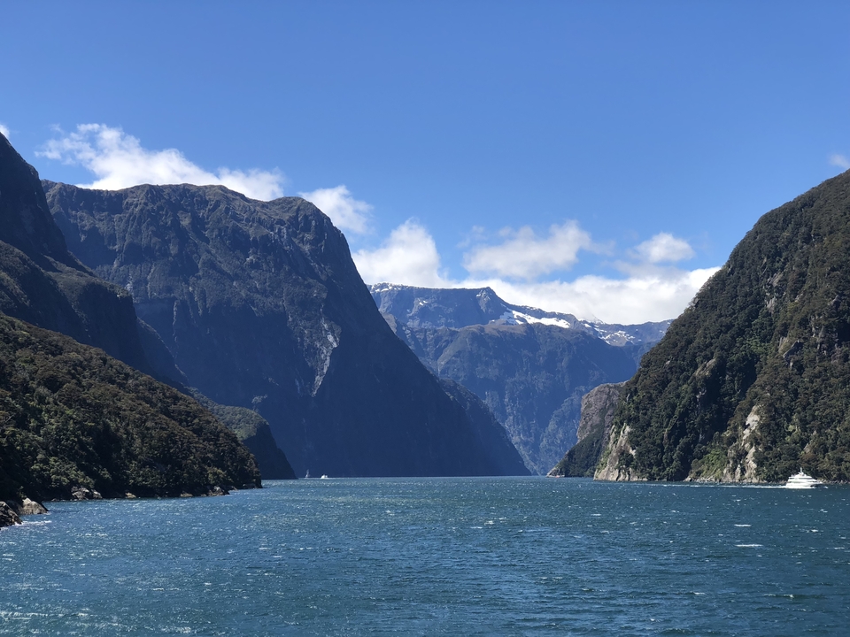 Wide view of a fjord with steep mountains under a blue sky.