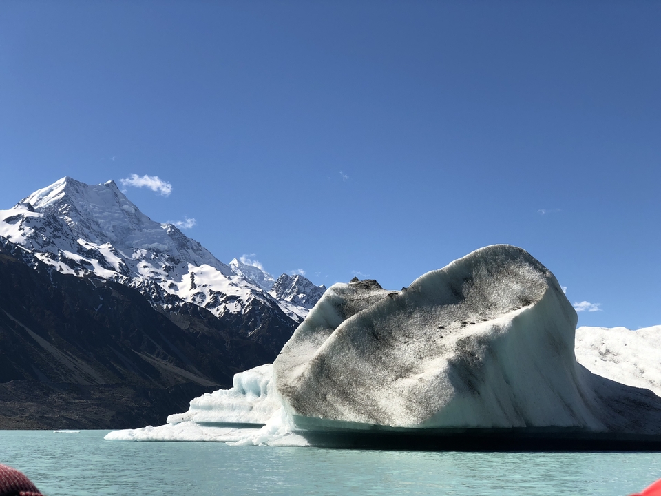 Large glacier with snowy mountains in the background on a sunny day.