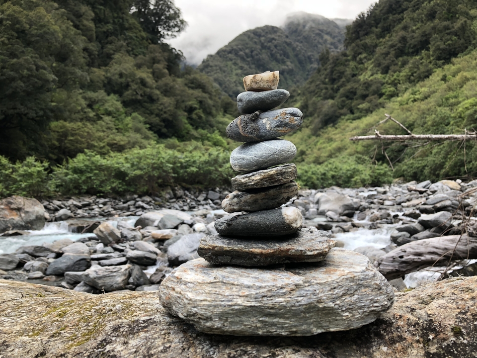 Pierres en équilibre dans un décor de rivière rocheuse entourée de forêt.