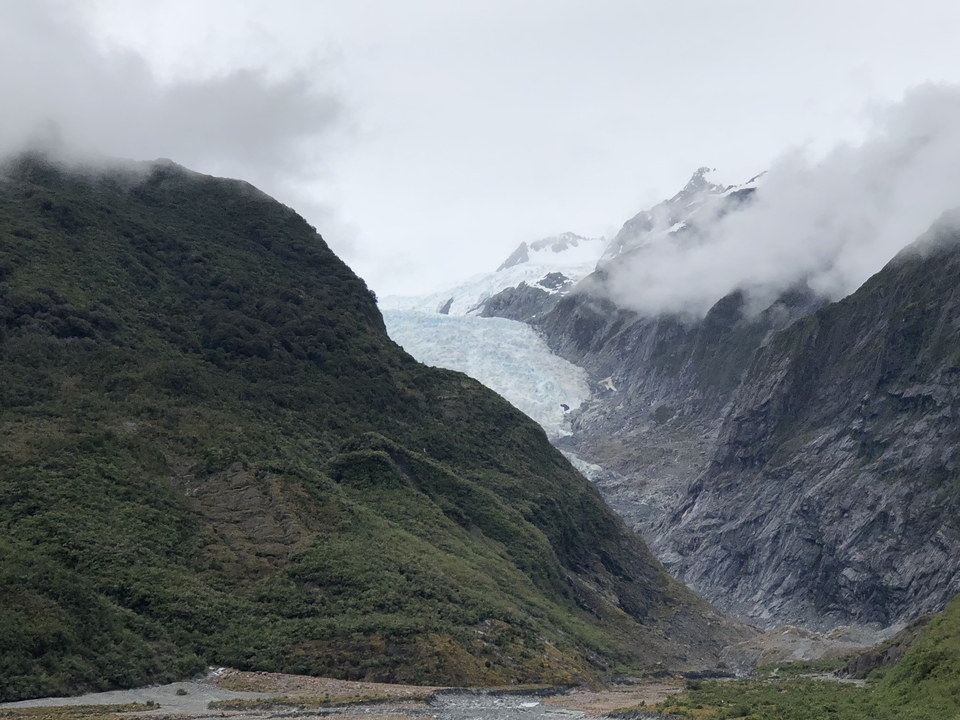 Glacier nestled between green mountains with a cloudy sky.