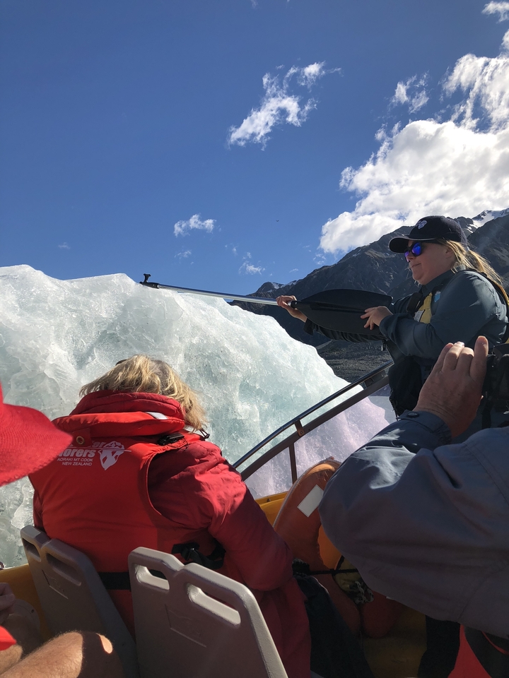 Des gens sur un bateau près d'un glacier, l'un d'eux pointant une pagaie vers la glace.