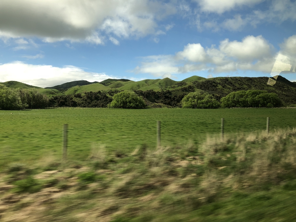 Collines verdoyantes sous un ciel partiellement nuageux vues depuis un véhicule en mouvement.