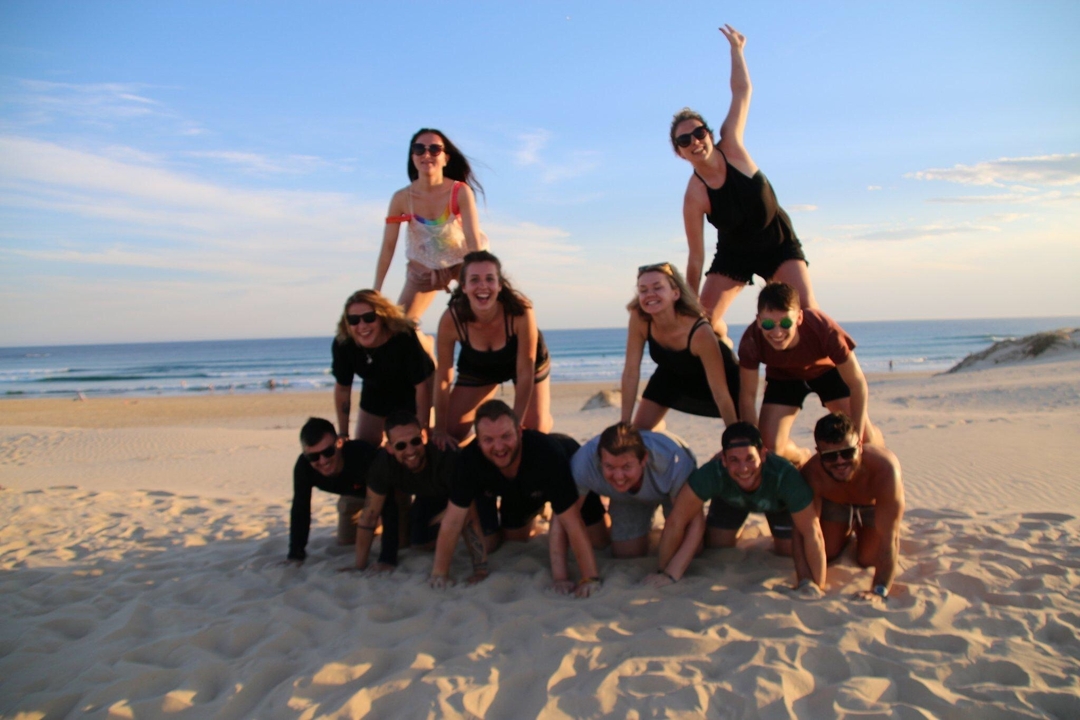 Group of friends making a human pyramid on a sandy beach.