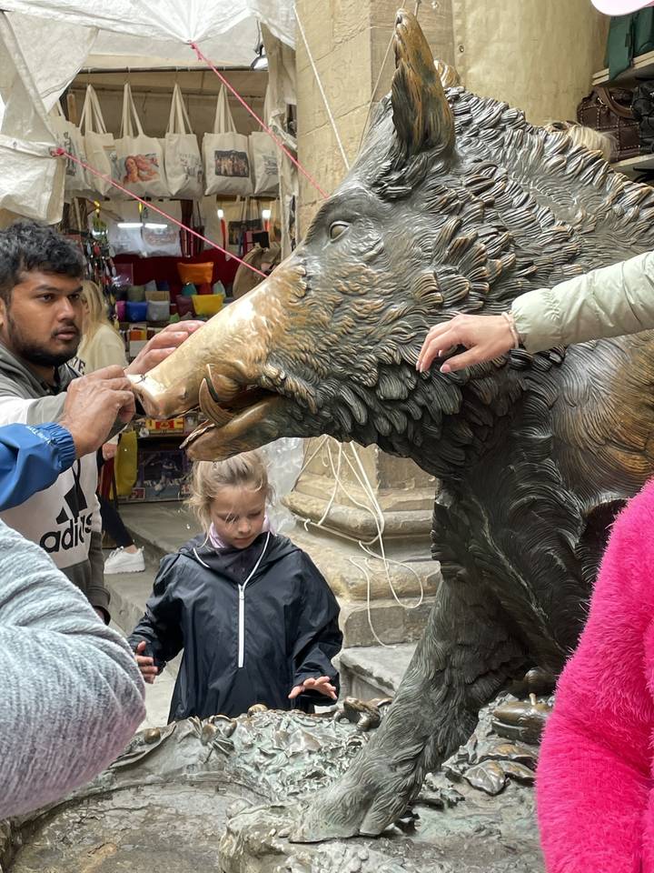 Une sculpture d'un sanglier avec des gens qui touchent son museau dans une zone de marché.