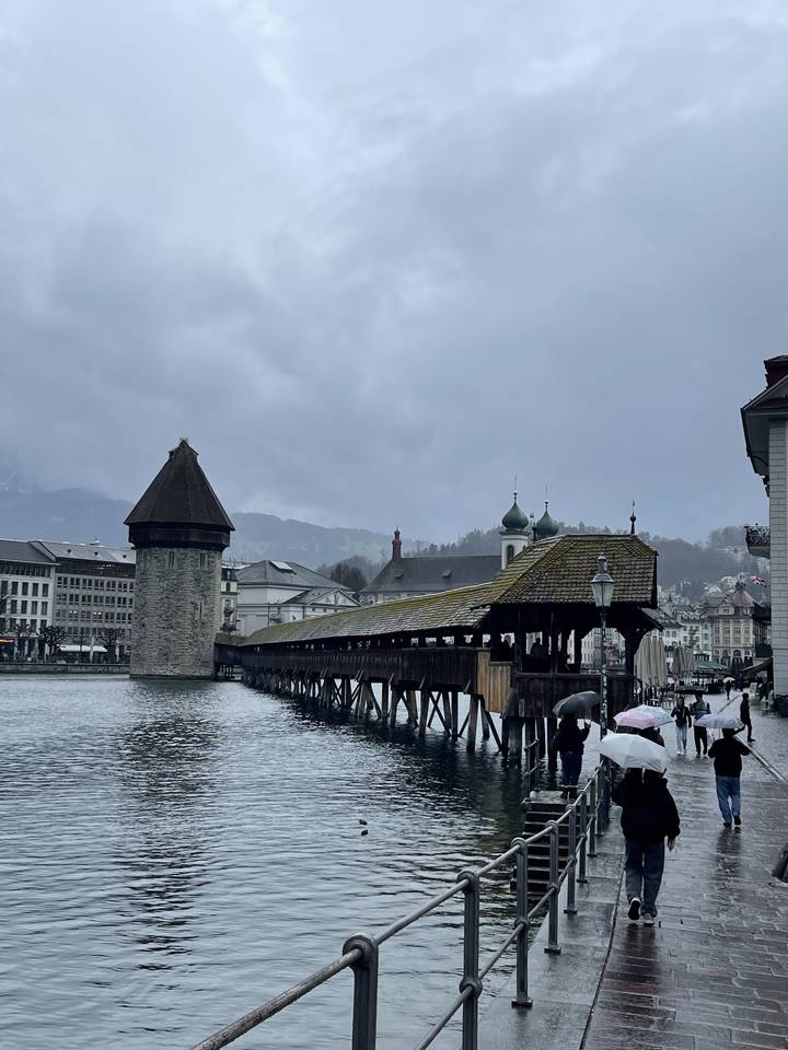 Des gens qui marchent sur un pont en bois par une journée pluvieuse avec de l'eau en dessous.