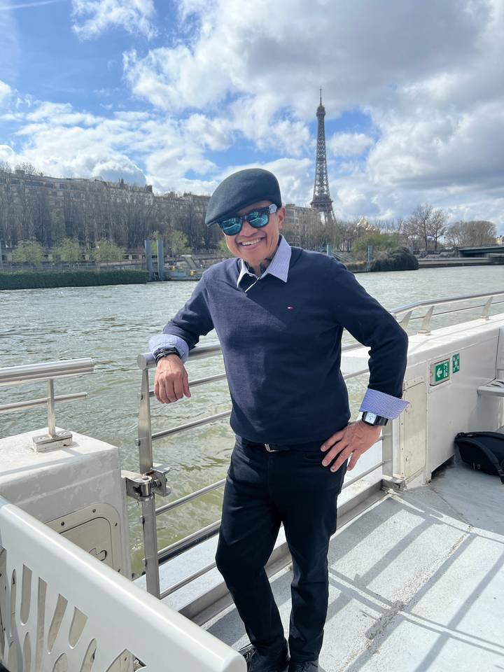 Personne posant sur un bateau fluvial avec la tour Eiffel en arrière-plan.