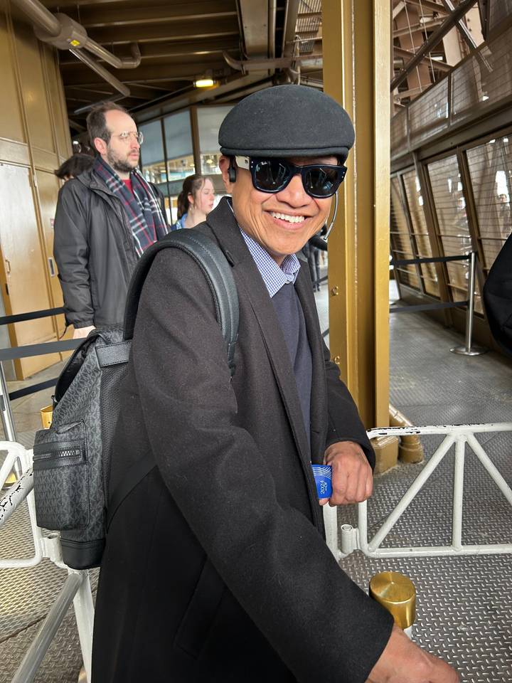 Personne souriante portant un chapeau et des lunettes de soleil faisant la queue.