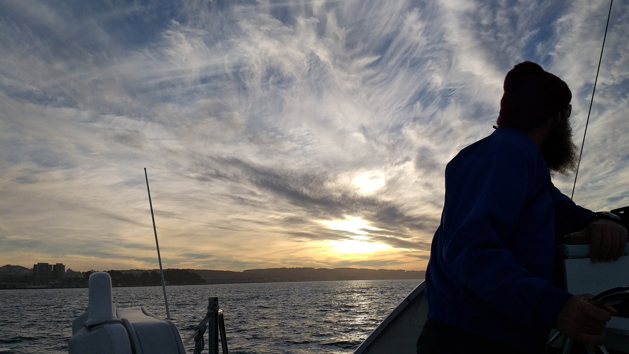 Une personne regardant au loin sur la mer au coucher du soleil depuis un bateau.