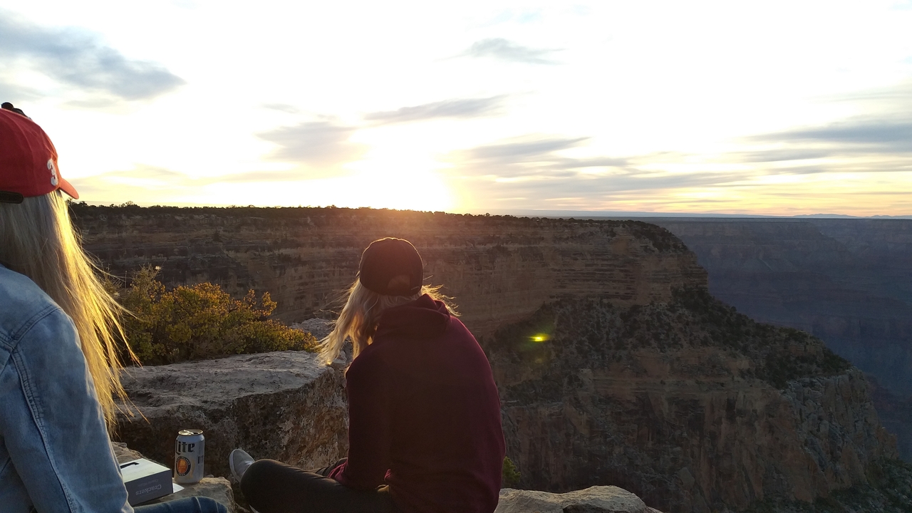 Deux personnes assises au bord d'un canyon au coucher du soleil.