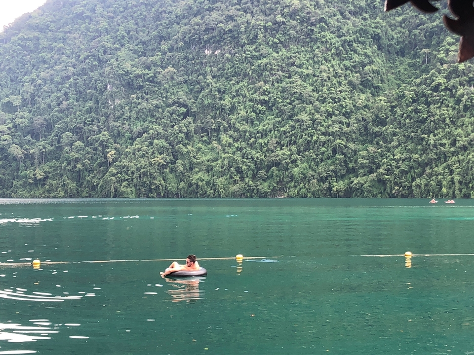 Person relaxing in an inner tube on a calm lake with lush green trees.