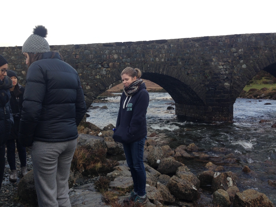 Group of people standing beside a stone bridge over a stream.
