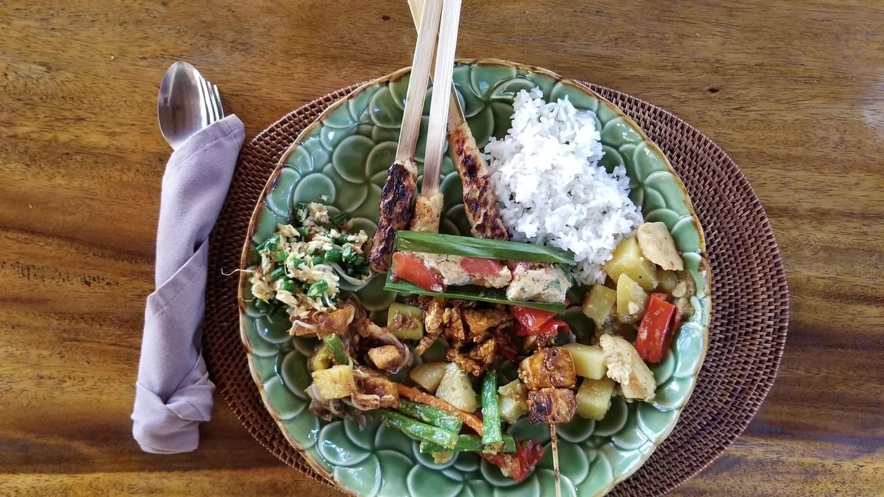 Une assiette de nourriture indonésienne variée avec du riz et des brochettes.