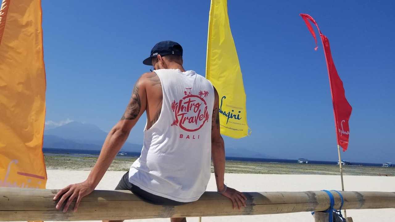 Homme assis sur une rambarde de plage avec des drapeaux colorés derrière.