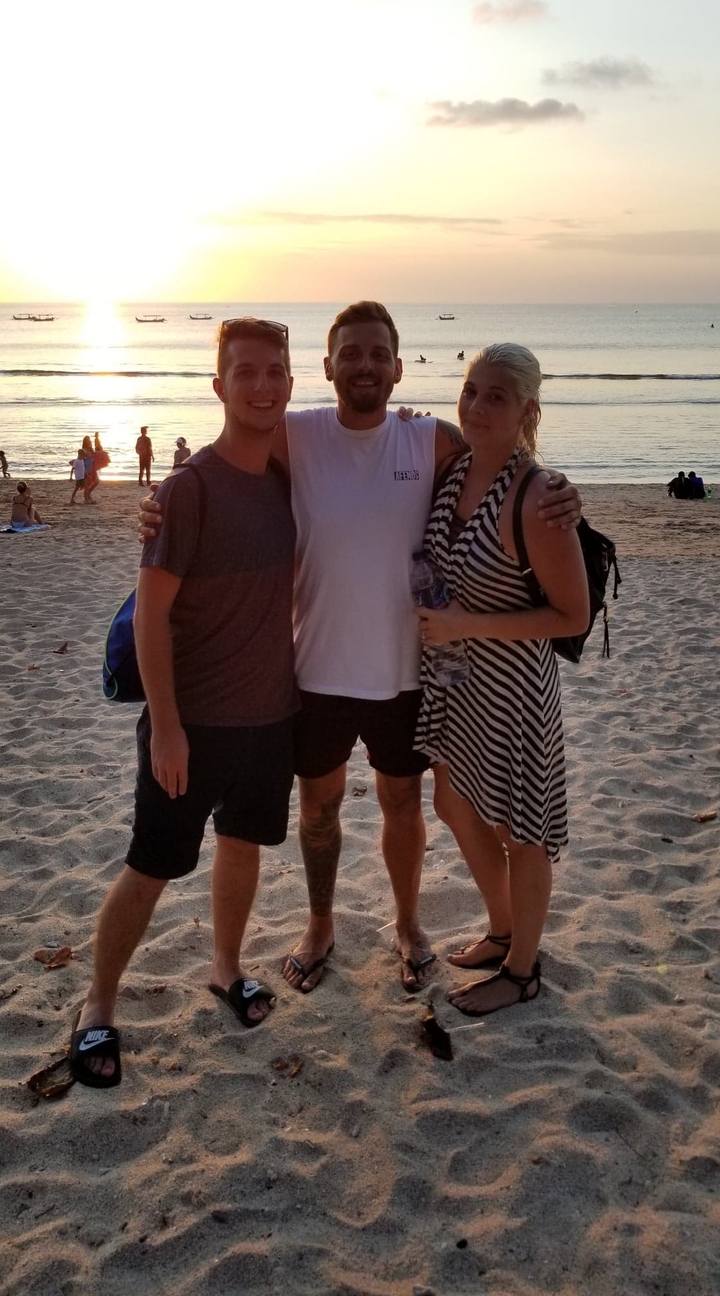 Trois personnes posant joyeusement sur une plage au coucher du soleil.