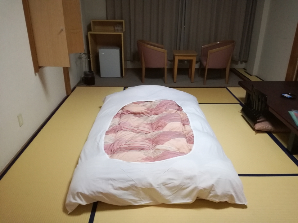 Chambre de style japonais avec un lit futon et des chaises.