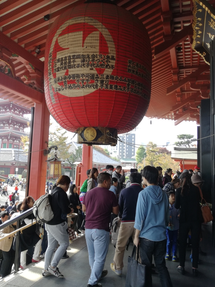 Foule de gens dans un temple sous une grande lanterne rouge.