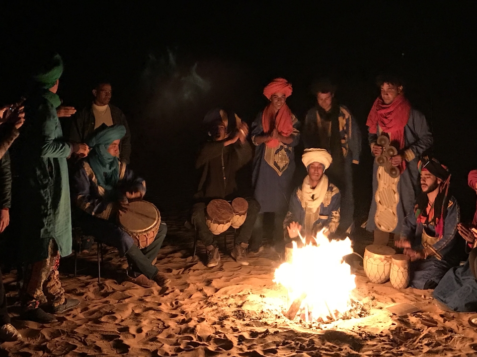 Groupe de personnes en tenues colorées jouant de la musique autour d'un feu de joie.