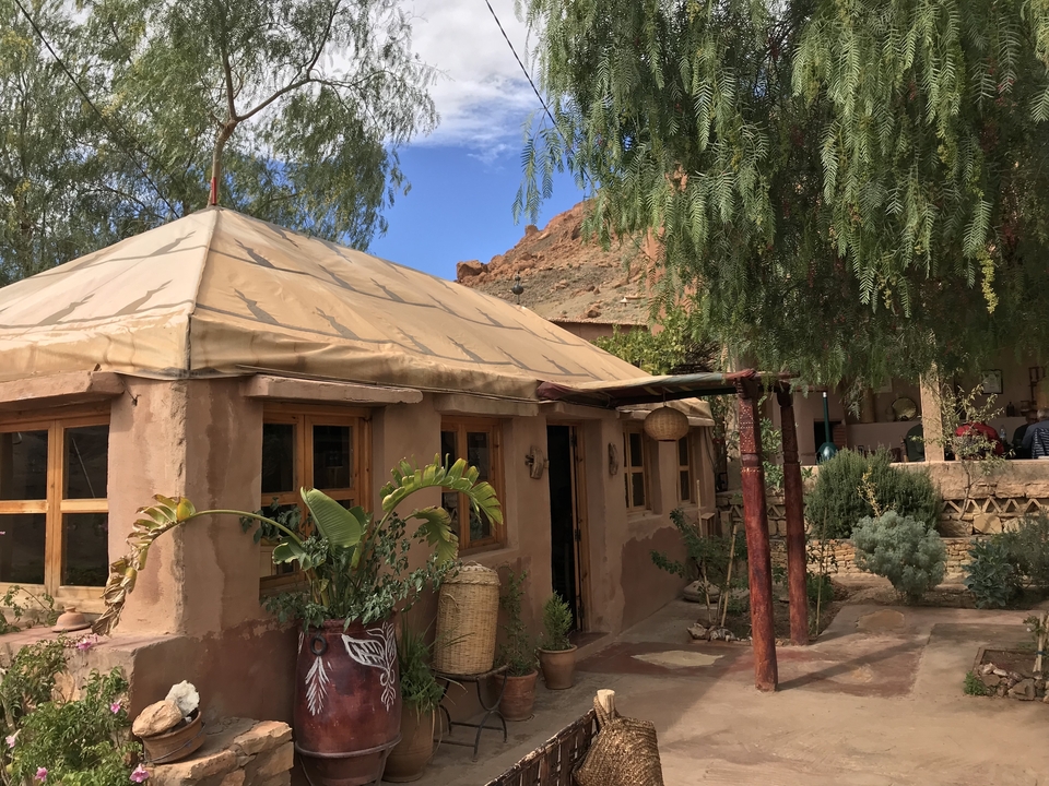Un bâtiment traditionnel en argile avec des plantes et un sentier de terre devant.