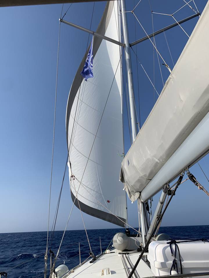 Sailboat with a white sail against a clear blue sea.