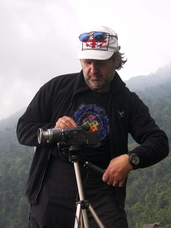 Un homme utilisant une caméra vidéo avec un arrière-plan de montagnes brumeuses.
