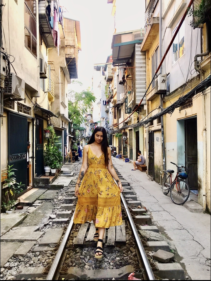 Personne en robe jaune marchant le long d'une rue urbaine étroite.