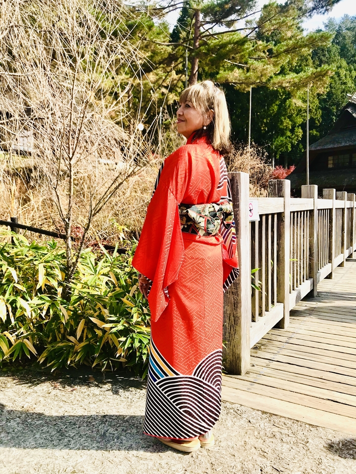 Femme en kimono rouge marchant sur un sentier en bois.