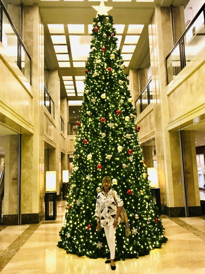 Femme debout devant un grand sapin de Noël dans le hall d'un hôtel.