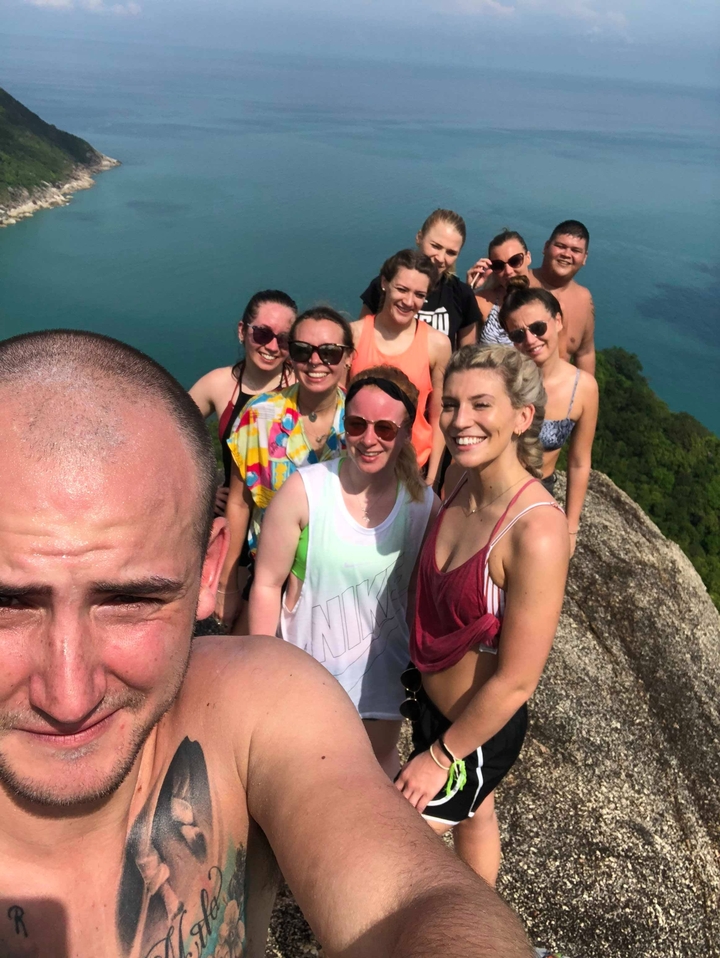 People posing at a scenic viewpoint with water and mountains.