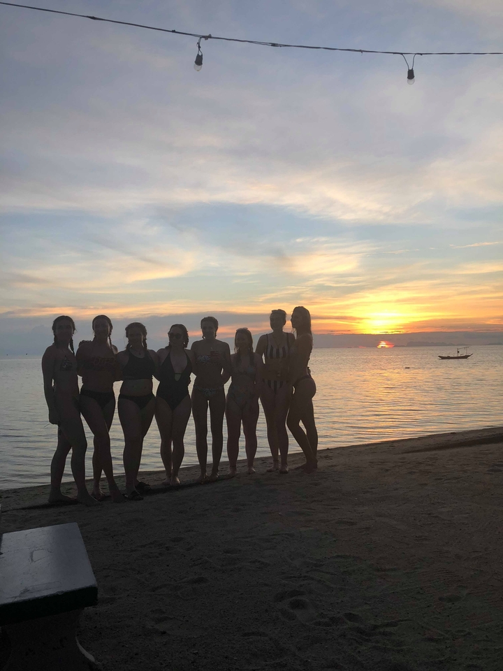 Group of people silhouetted against a sunset on the beach.