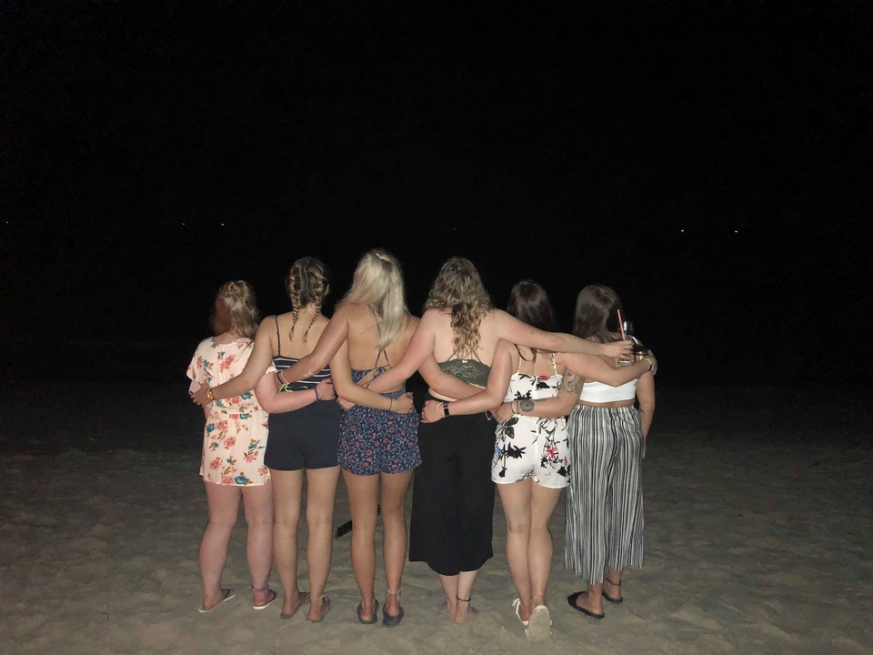 Groupe de femmes se tenant par les épaules la nuit sur une plage.