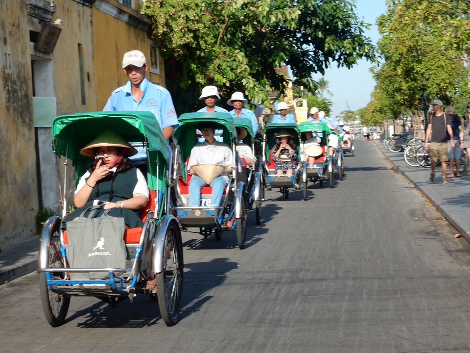 Groupe de personnes circulant en cyclo-pousses dans une rue ensoleillée.