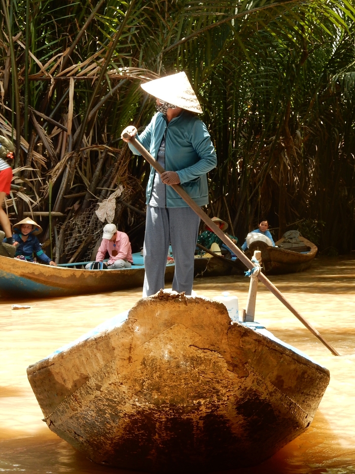 Personne debout sur un bateau avec d'autres en arrière-plan dans un décor fluvial.