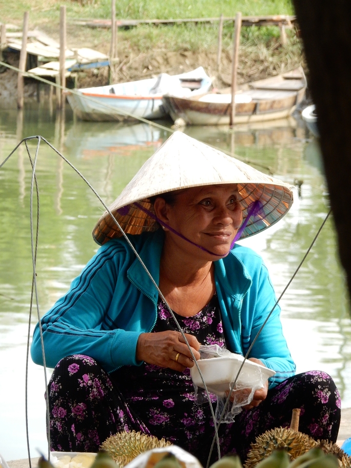 Femme souriante portant un chapeau conique assise à l'extérieur.