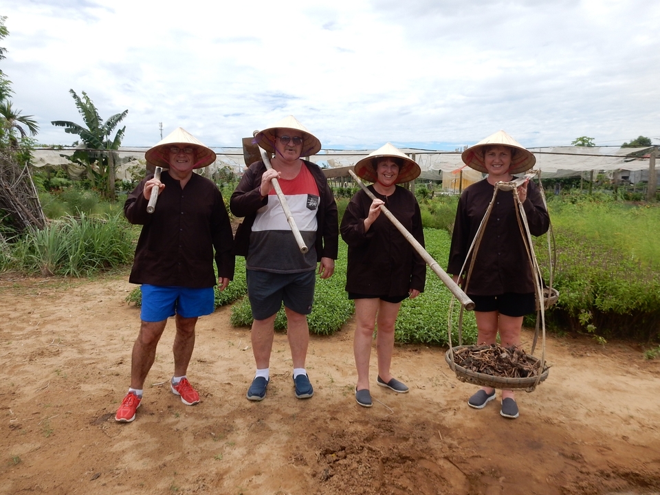 Groupe de touristes portant des chapeaux traditionnels et tenant des outils agricoles.
