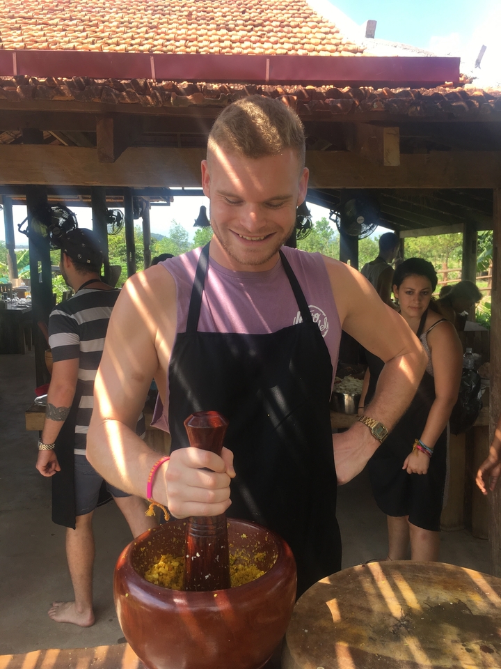 Personne tenant un outil traditionnel lors d'un cours de cuisine en plein air.
